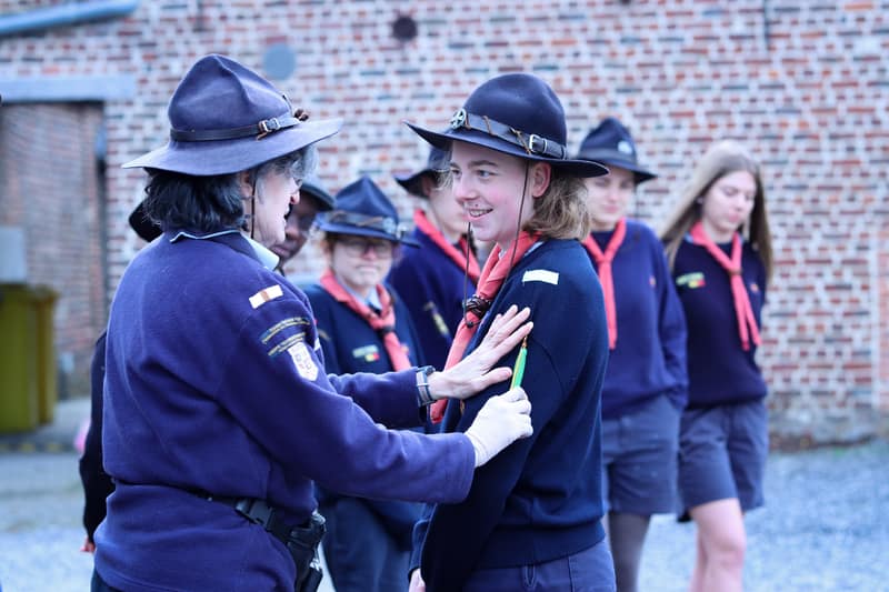 Een ervaren leidster helpt een jongere leidster met haar uniform tijdens een plechtigheid.